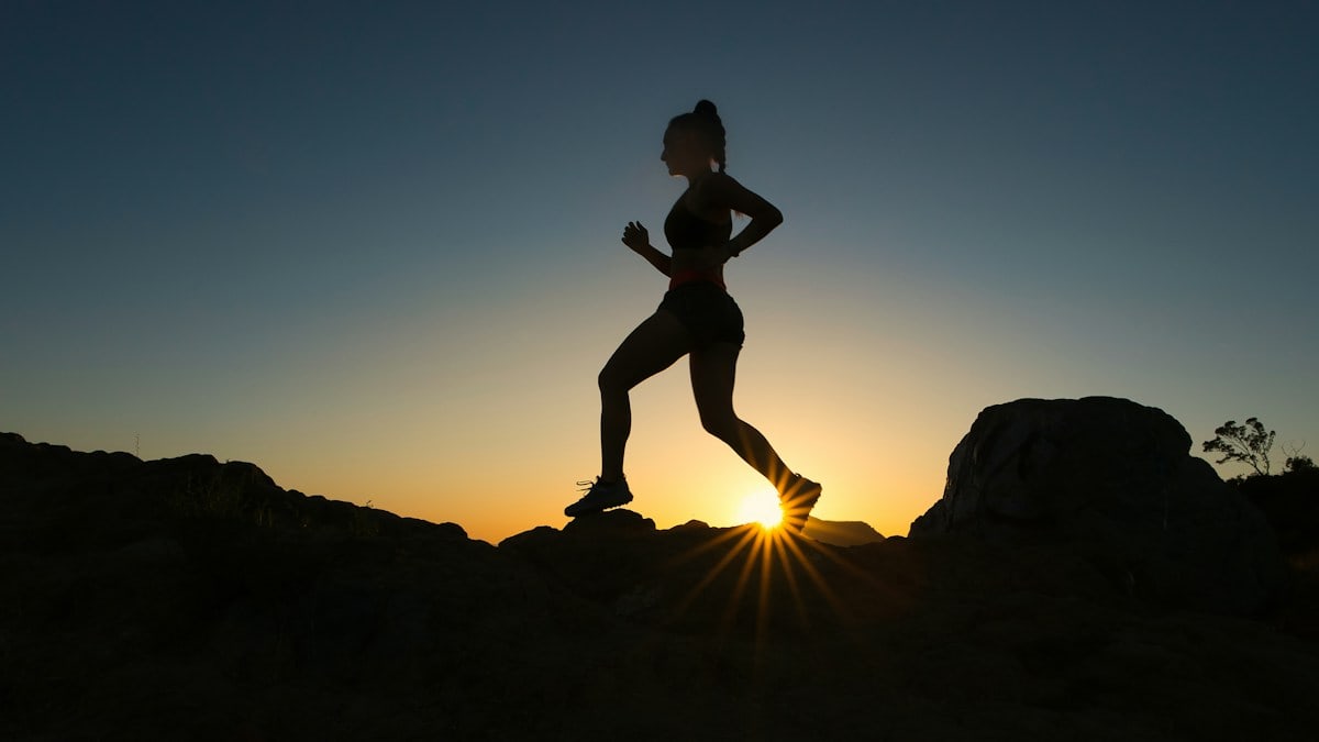 A woman runs up a trail during sunset.